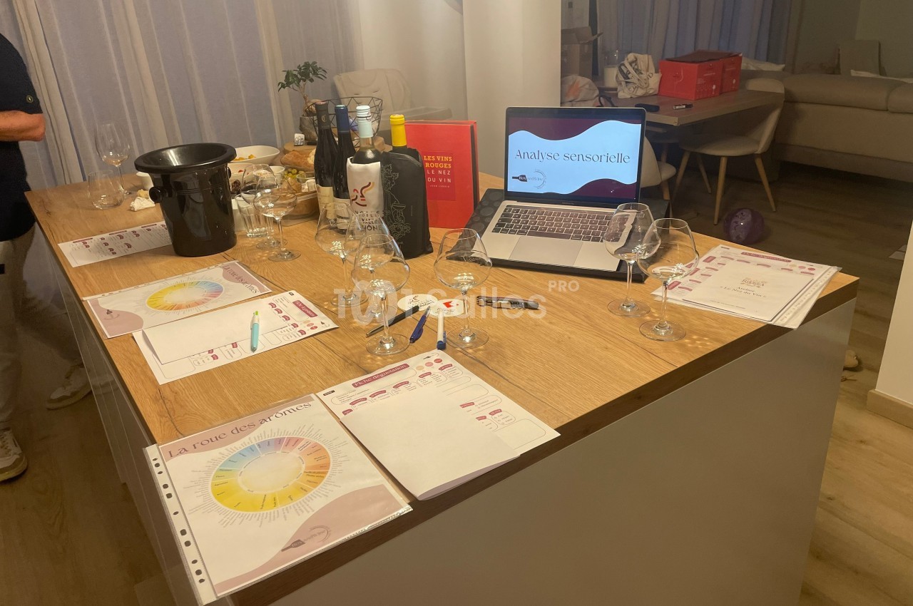 Table en bois avec verres, bouteilles de vin, documents d'analyse sensorielle et ordinateur affichant une présentation.