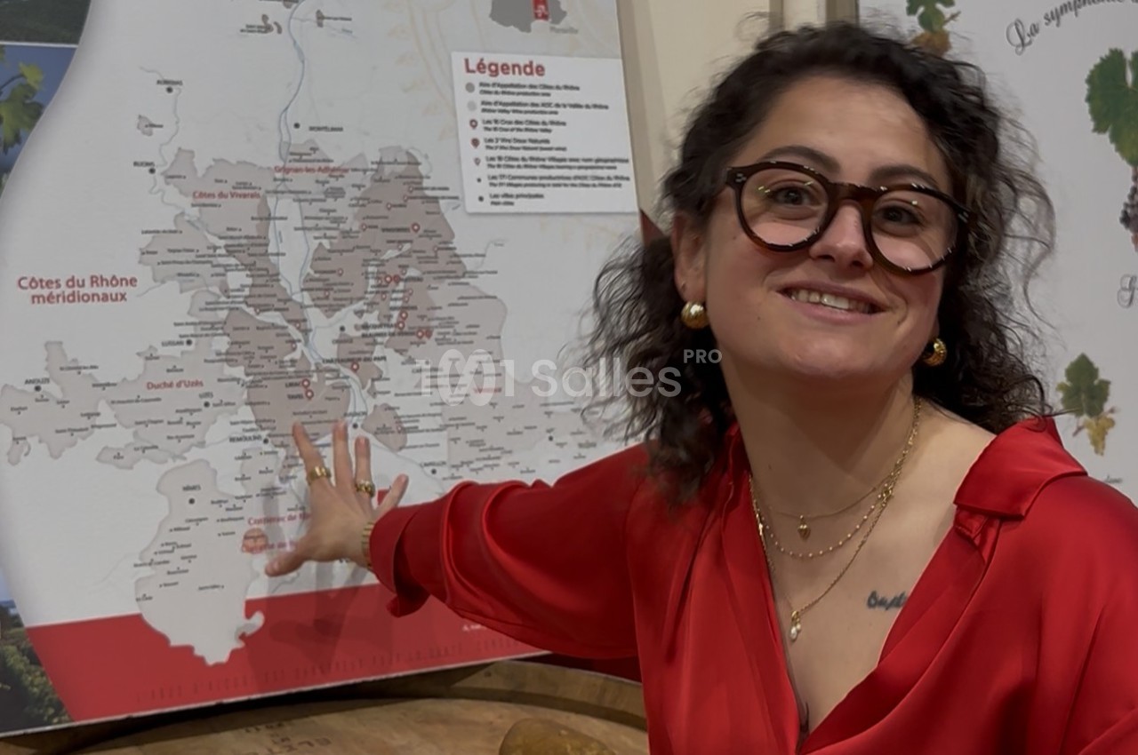 Femme en chemisier rouge montrant une carte des Côtes du Rhône méridionales sur un panneau explicatif.