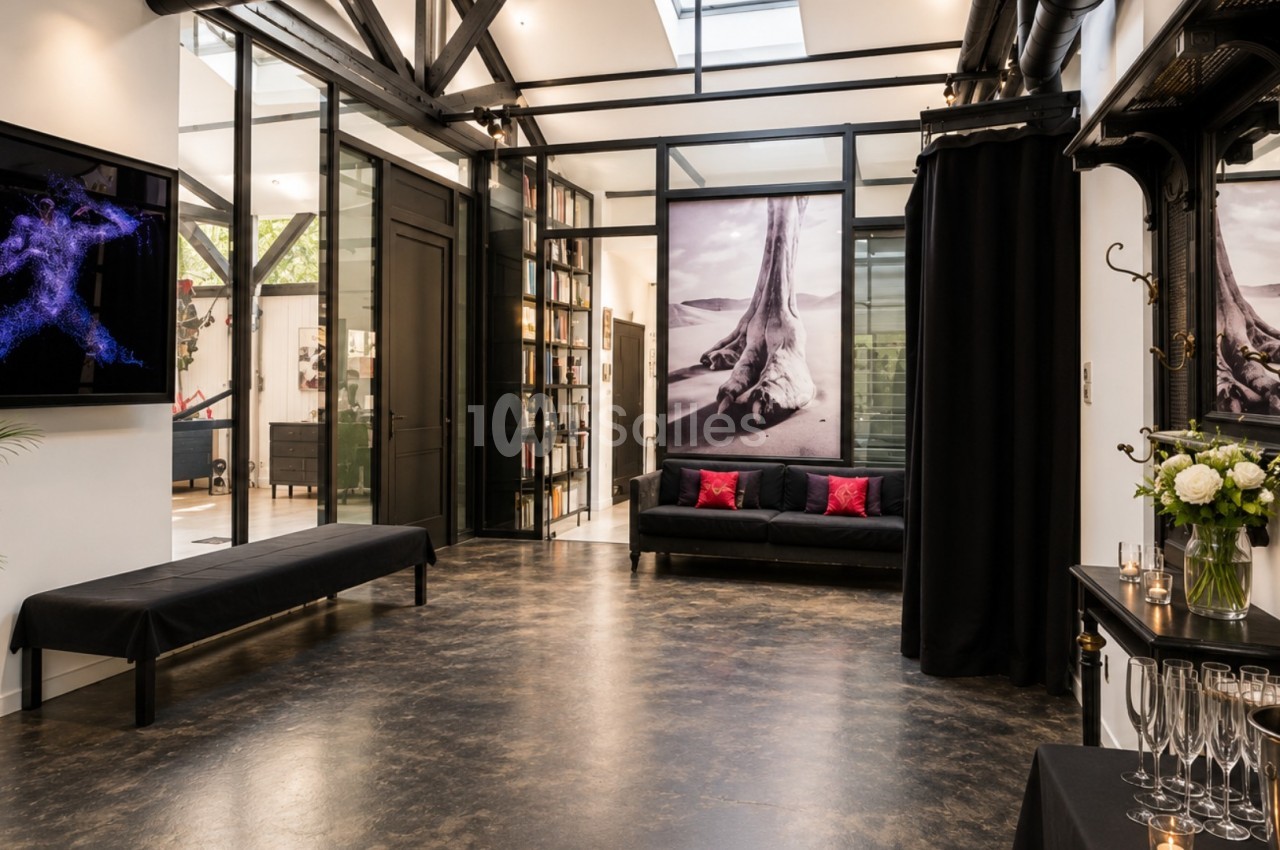 Espace intérieur moderne avec sol en béton, canapé noir, œuvres d'art murales et table avec flûtes de champagne.