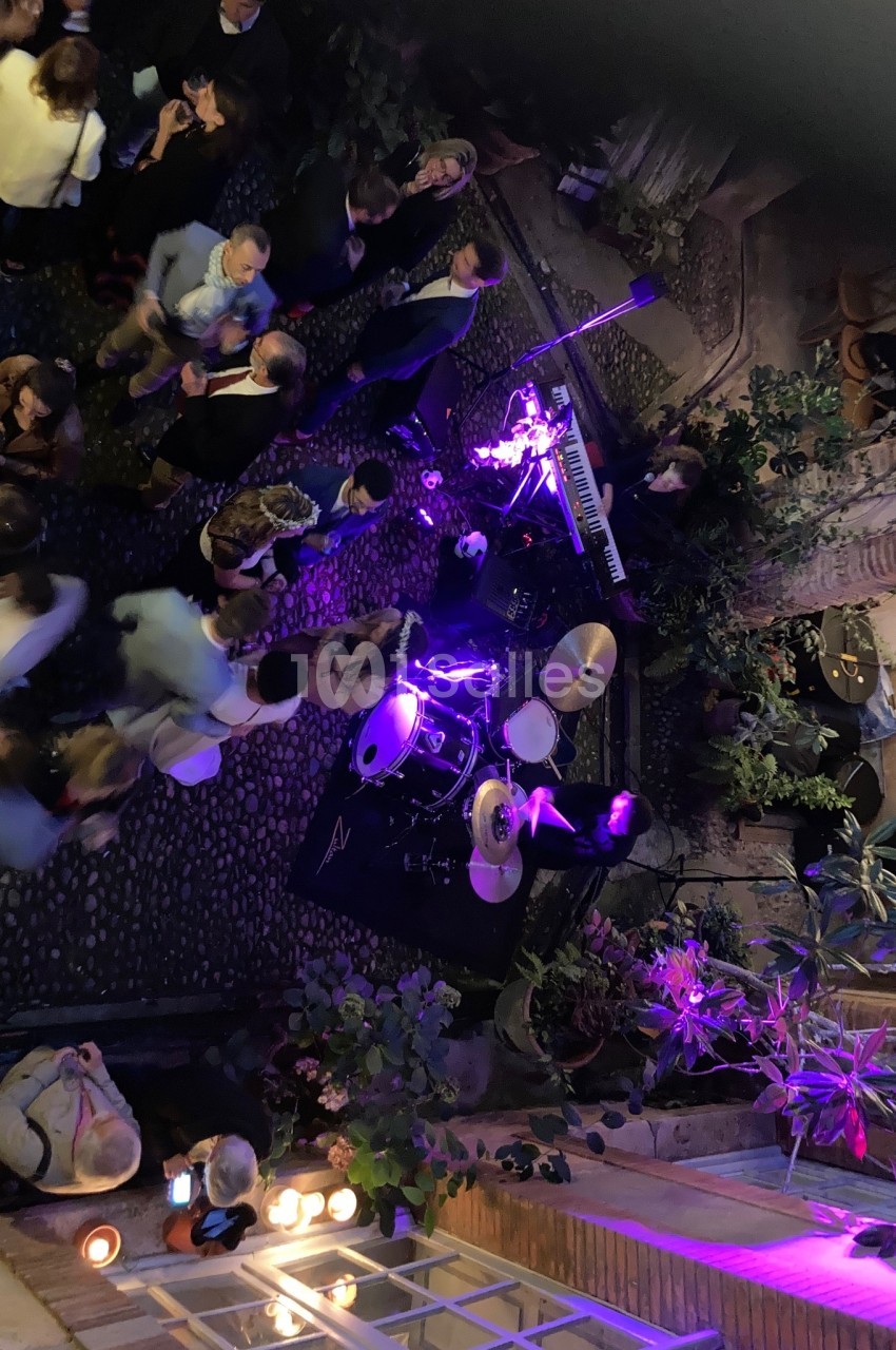 Vue aérienne d'une scène musicale en extérieur avec batterie, clavier et éclairage violet, entourée de spectateurs.