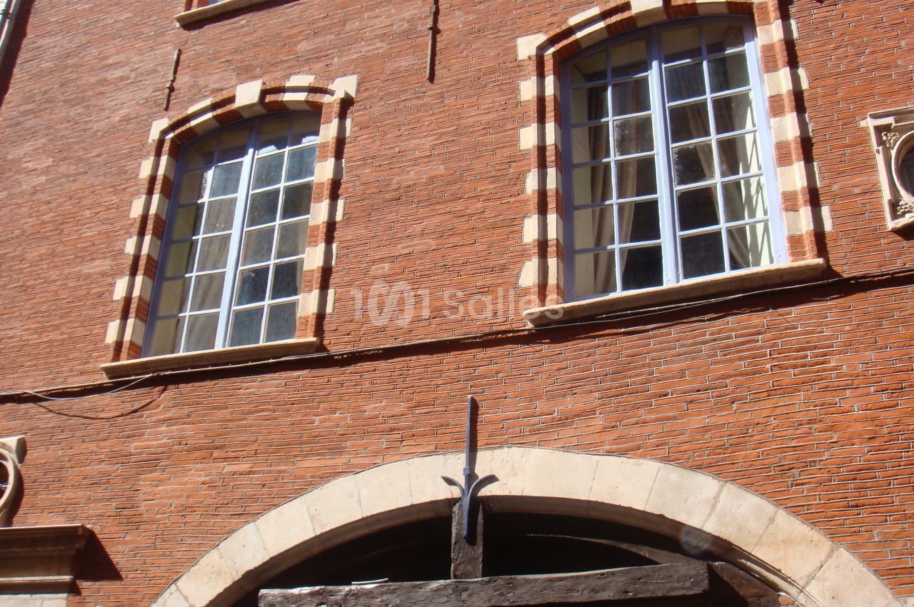 Façade en briques rouges avec fenêtres à encadrement clair et arc en pierre au-dessus d'une porte en bois.