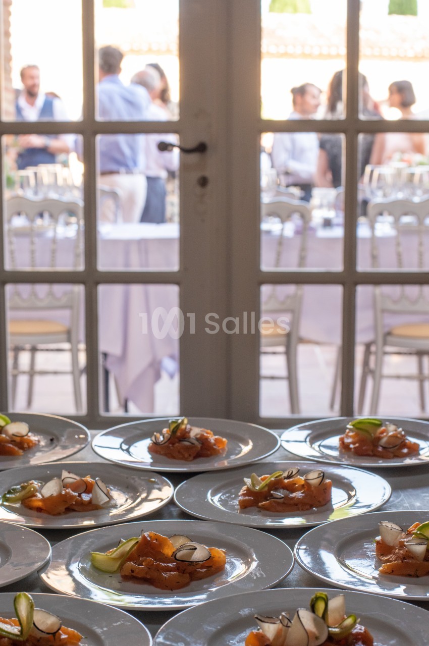 Assiettes de saumon fumé garnies de légumes, disposées sur une table devant une porte vitrée donnant sur une réception.