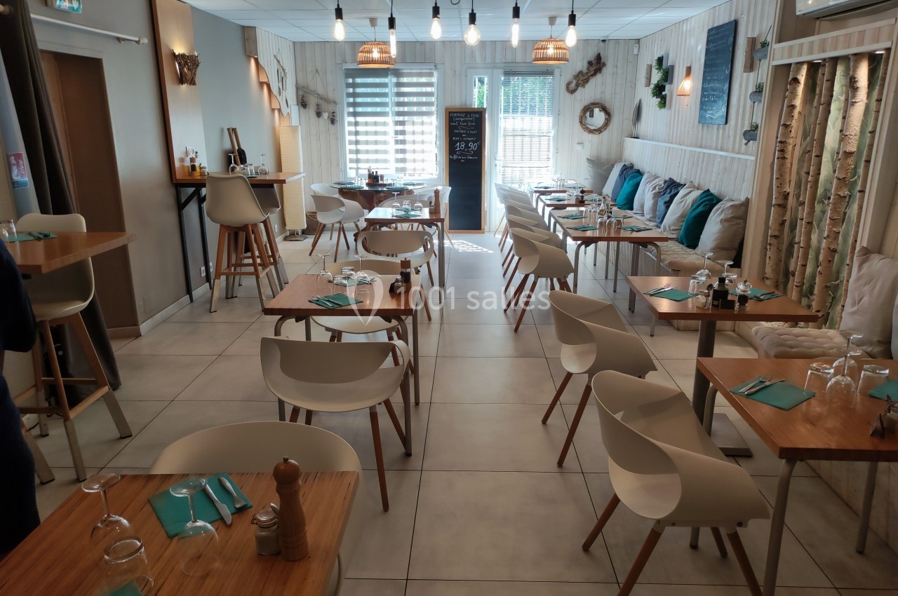 Salle de restaurant lumineuse avec tables en bois, chaises blanches et décoration naturelle sur les murs.