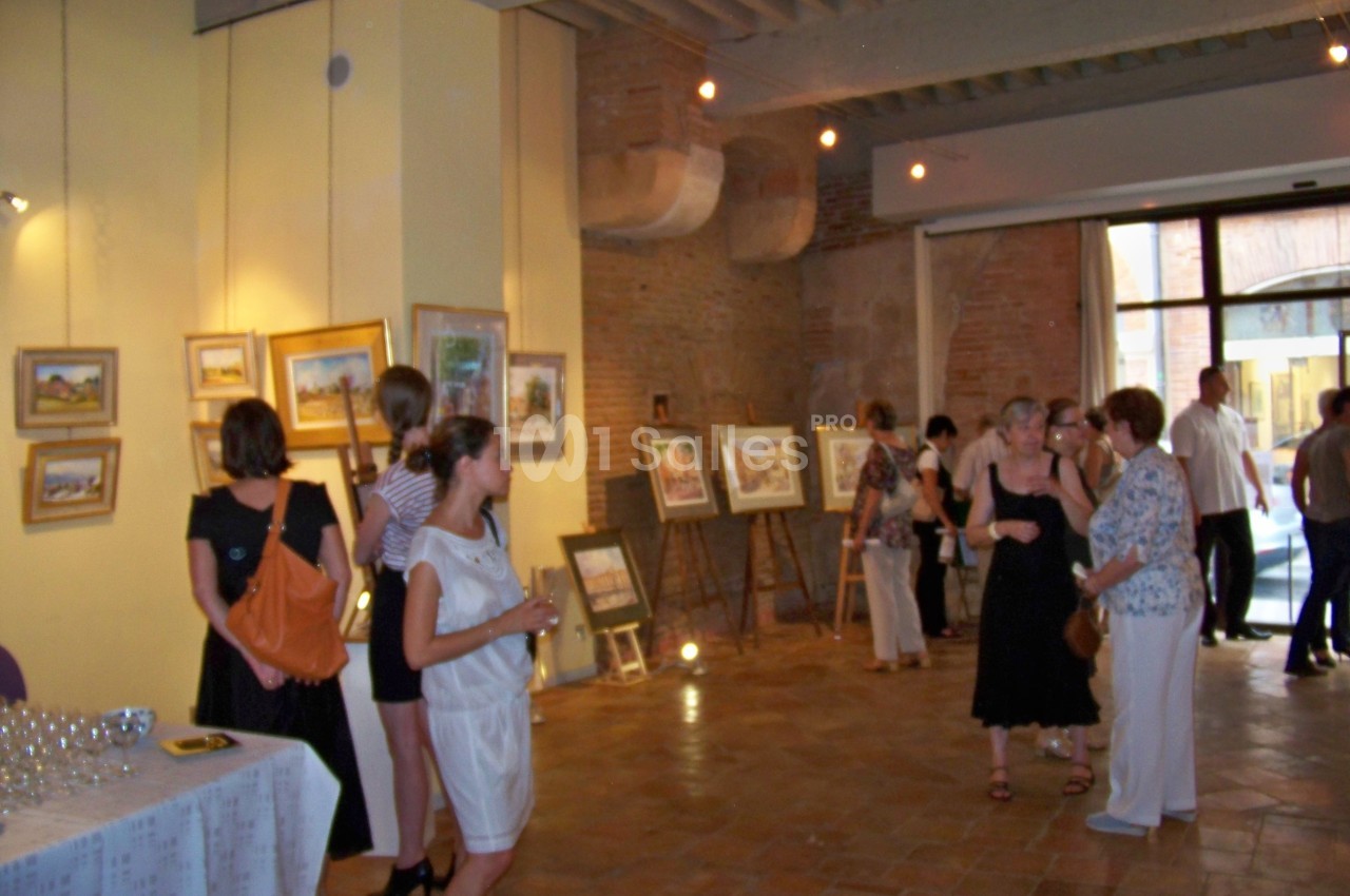 Des personnes visitent une exposition d'art dans une salle avec des peintures accrochées aux murs et posées sur des…