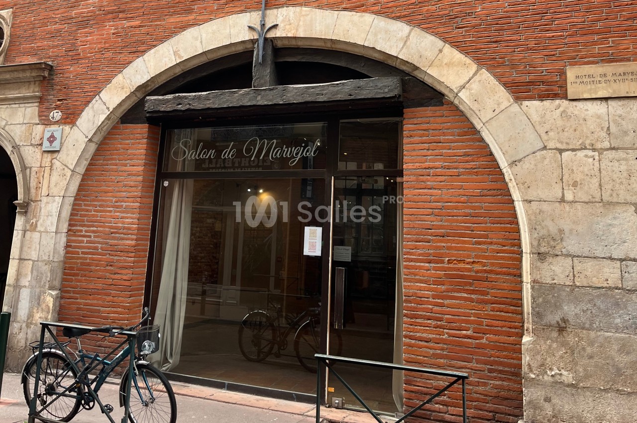 Façade en briques rouges d'un salon avec une grande vitrine et une arche en pierre, deux vélos stationnés devant.