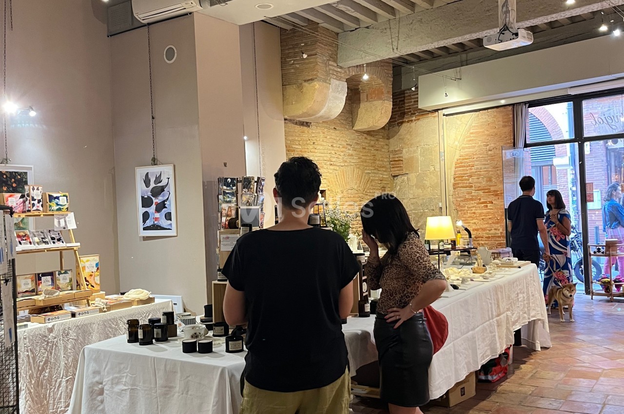 Deux personnes regardent des produits artisanaux sur des tables dans une boutique à l'intérieur d'un bâtiment en briques.