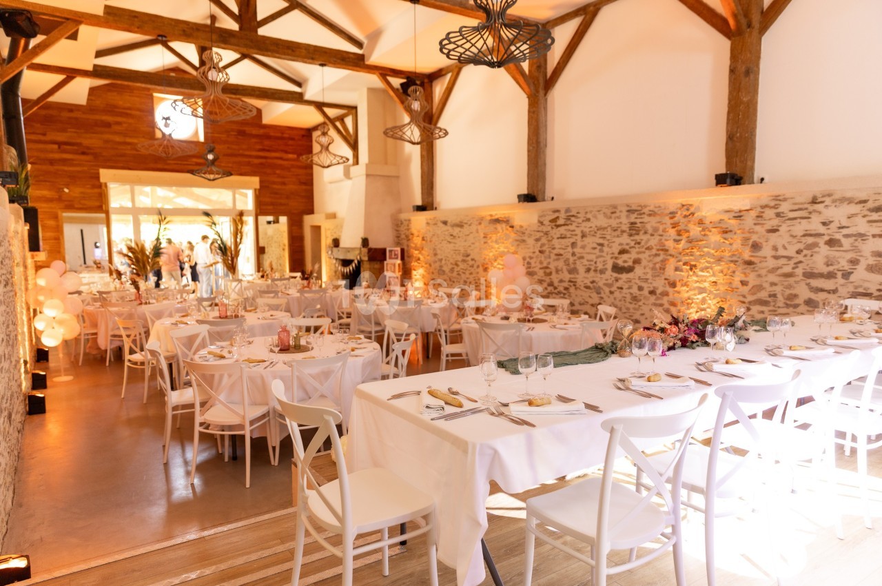 Salle intérieure avec tables rondes dressées, chaises blanches et murs en pierre - ambiance chaleureuse.