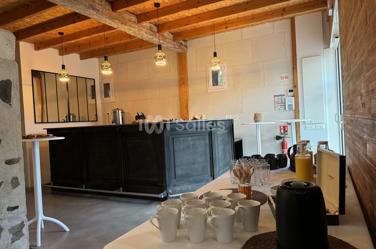 Espace de réception avec bar bleu-gris, poutres apparentes, pendentifs dorés et table de service avec tasses et théière.