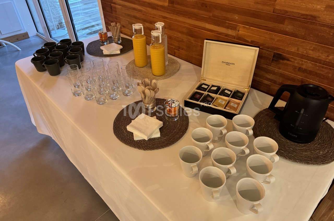 Table blanche dressée avec verres, tasses, mugs noirs, bouteilles de jus de fruit et boîte de thé Dammann.