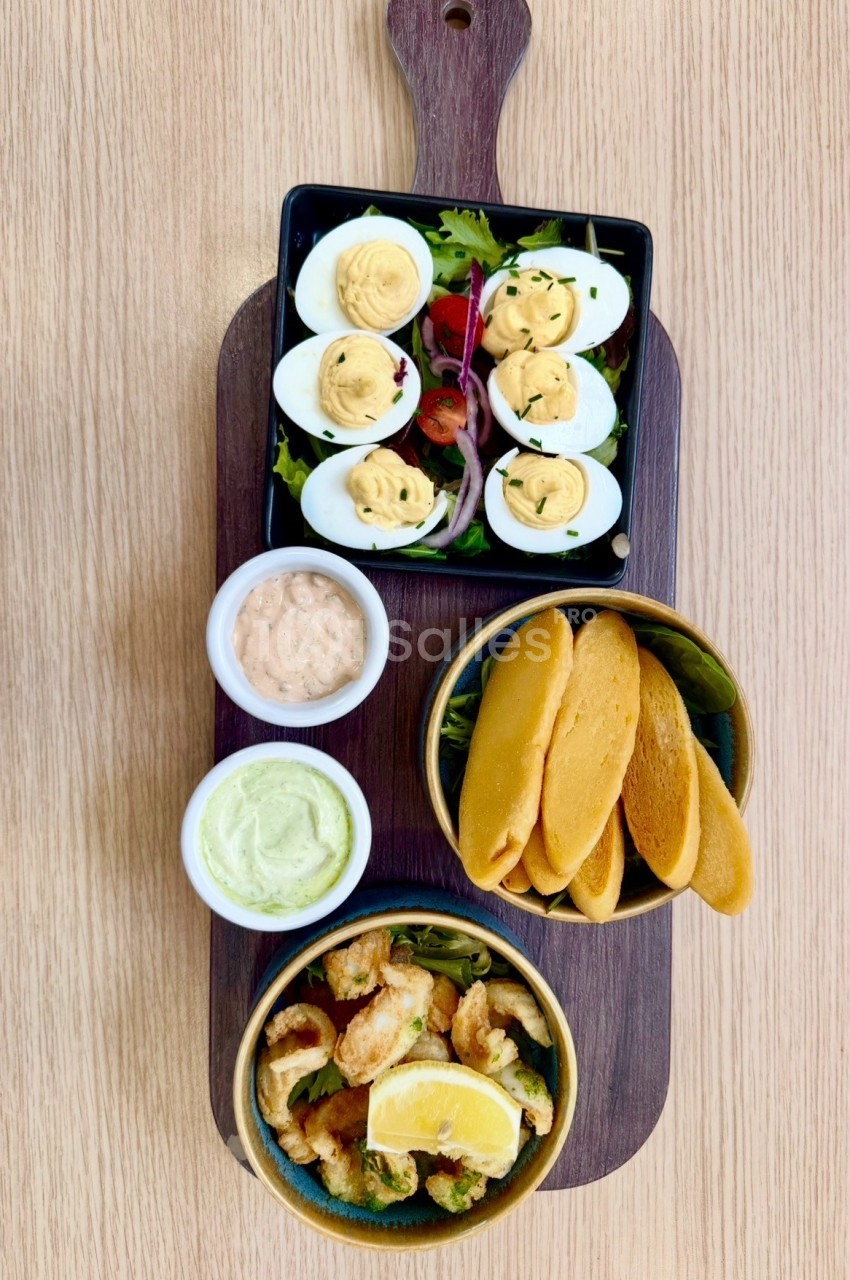 Planche de dégustation avec œufs farcis, sauces, crêpes et crevettes frites sur bois.