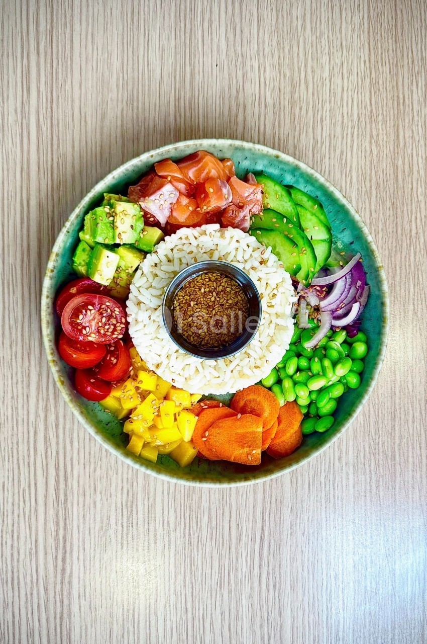 Assiette de riz blanc entouré de légumes colorés - concombre, tomate, poivron, carotte, petits pois - et sauce au centre.