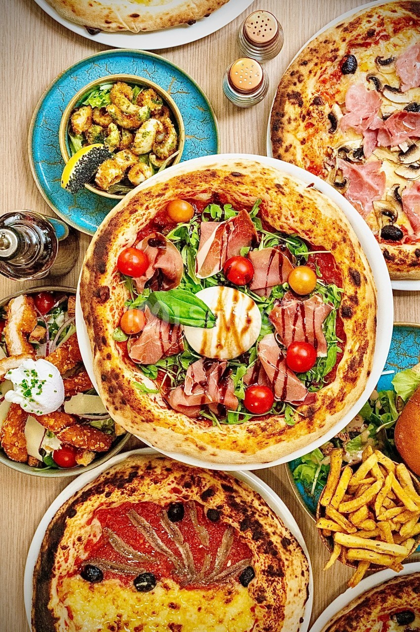 Plusieurs pizzas garnies de jambon, tomates cerises et roquette, accompagnées de crevettes et frites.