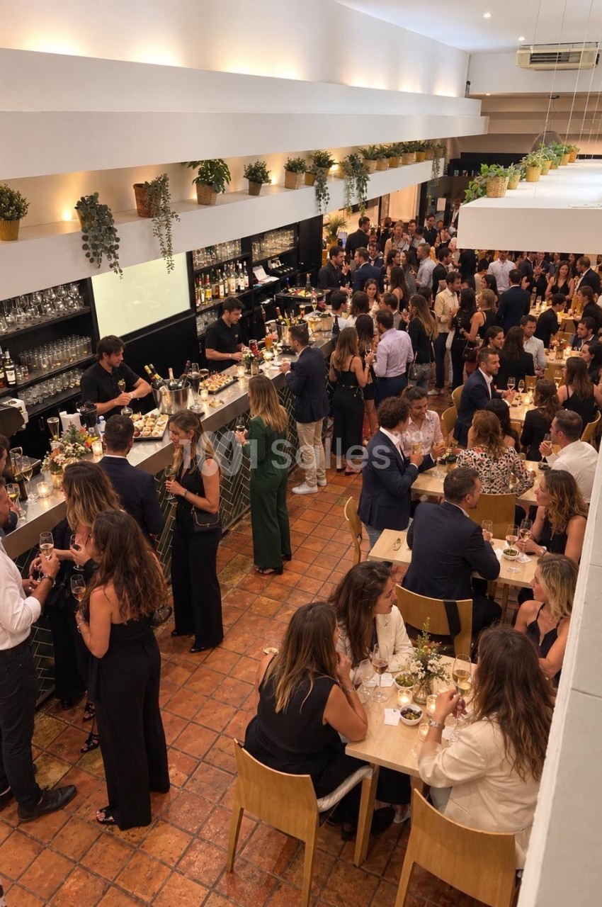 Salle intérieure avec bar noir, plantes suspendues éclairées, convives attablés et debout lors d'un événement.