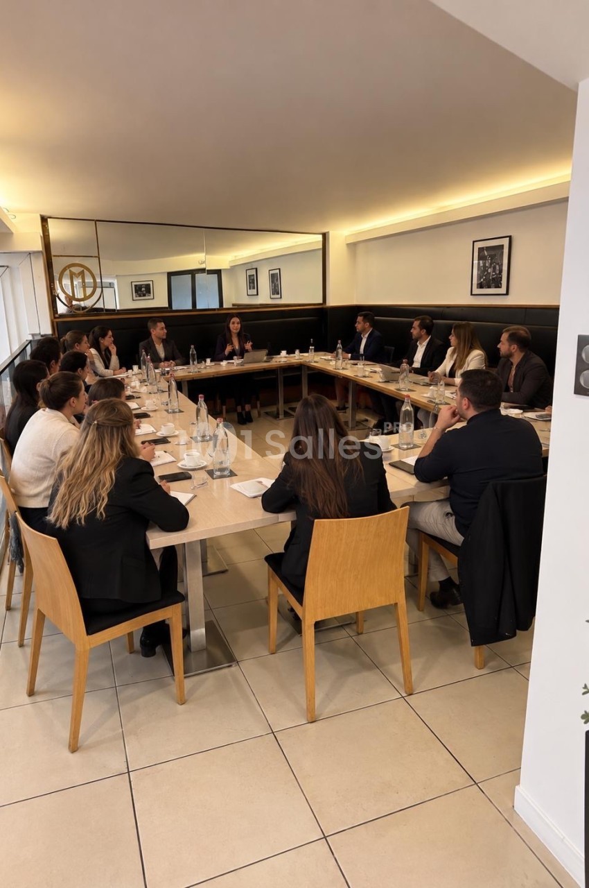 Salle de réunion avec table en U - environ 20 personnes en costume autour d'une table en bois.