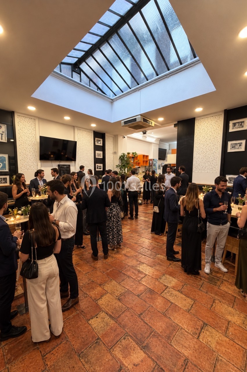 Salle intérieure avec puits de lumière, convives debout en tenue de soirée, sol en carrelage terracotta, murs noirs et blancs.