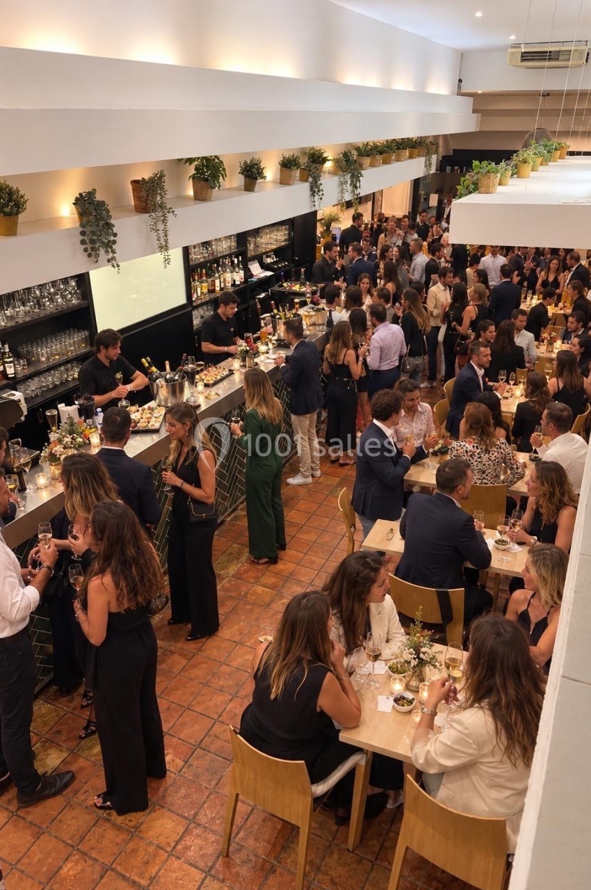 Salle intérieure avec bar noir, plantes suspendues éclairées, convives attablés et debout lors d'un événement.