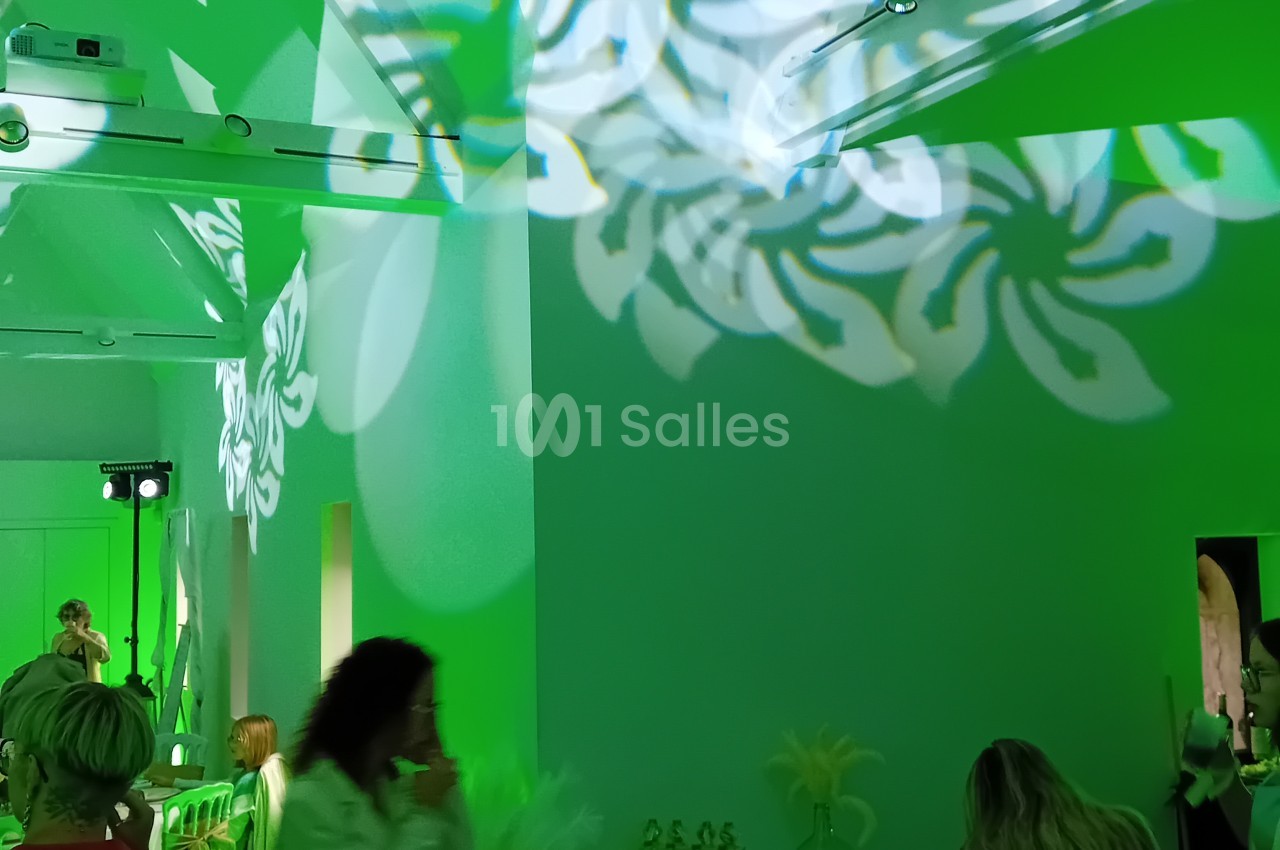 Espace intérieur aux murs vert fluo avec décoration florale suspendue, éclairage de scène et plusieurs personnes.