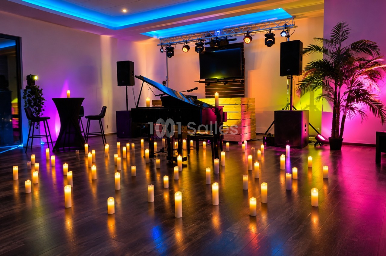 Salle aménagée avec piano, scène, éclairage multicolore bleu-orange-rose et bougies au sol.