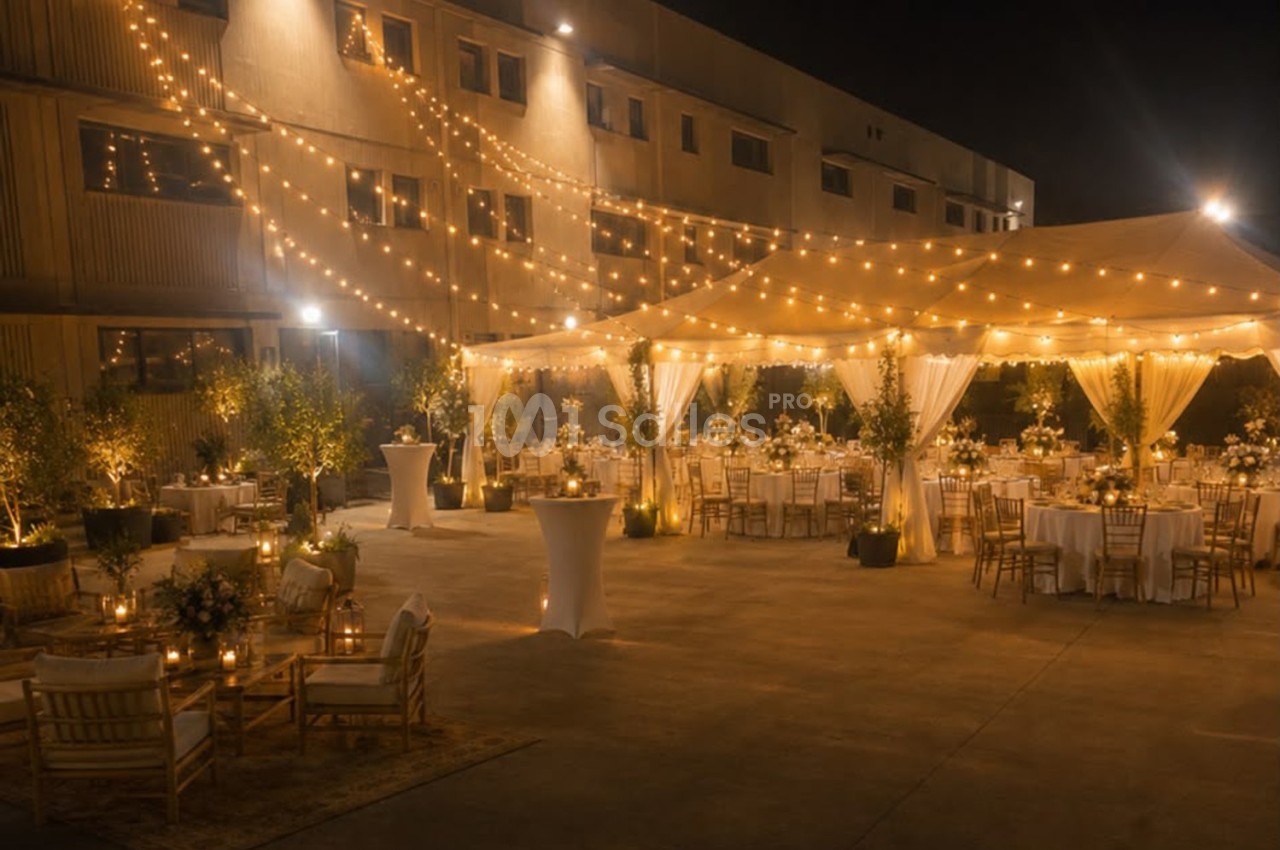 Cour extérieure éclairée la nuit avec des guirlandes lumineuses, des tables décorées et des chaises pour un événement.