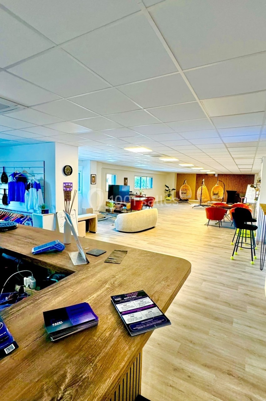 Espace lumineux avec comptoir en bois, coin salon, fauteuils suspendus et présentoirs de vêtements en arrière-plan.