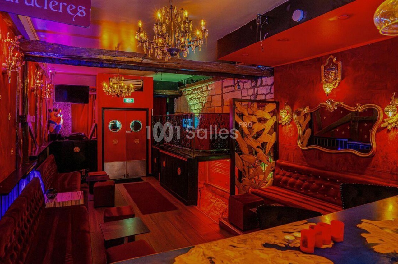 Intérieur d'un bar à l'ambiance chaleureuse avec murs rouges, lustres, banquettes et décorations élégantes.