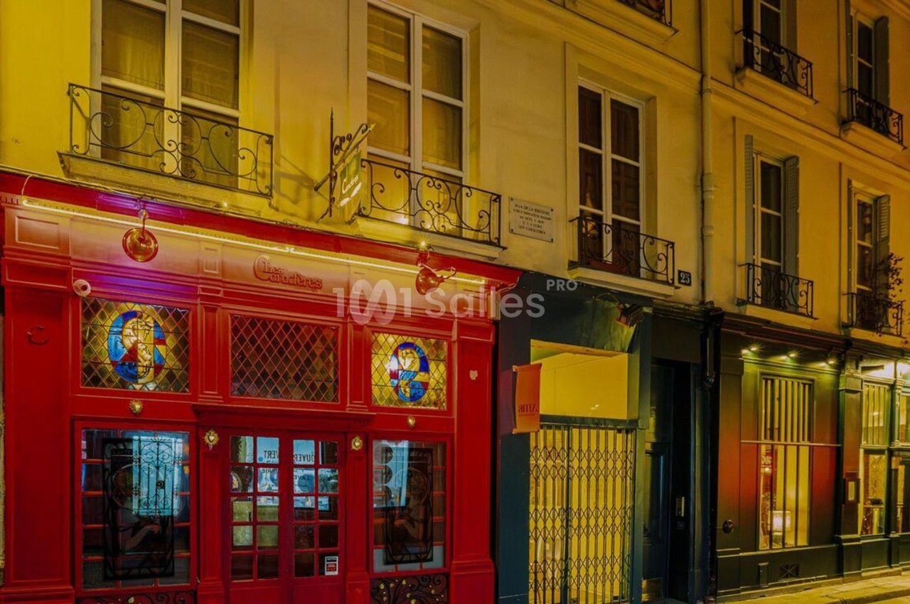 Façade de bâtiments colorés avec une devanture rouge ornée de vitraux, éclairée par des lumières nocturnes.