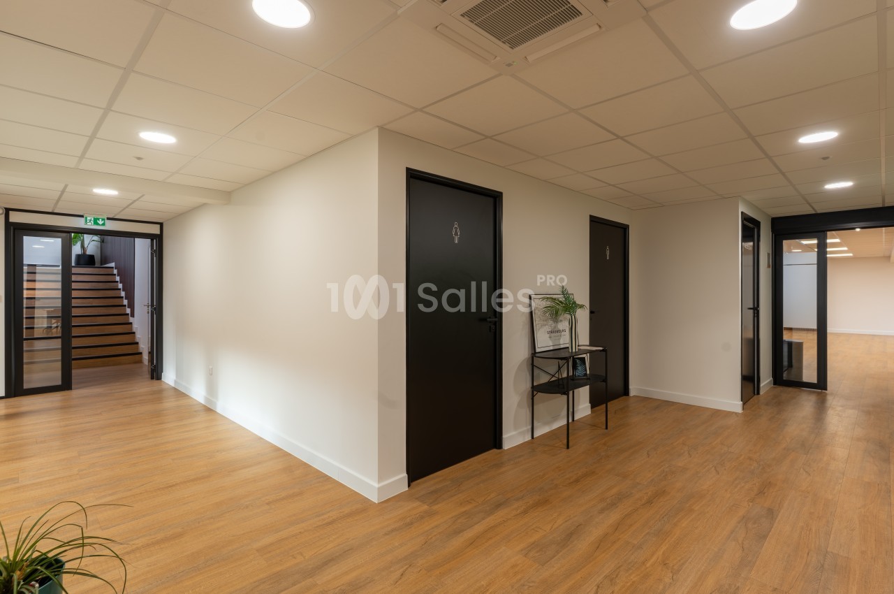 Espace intérieur vide avec sol en parquet, murs blancs, portes noires et éclairage de plafond encastré.