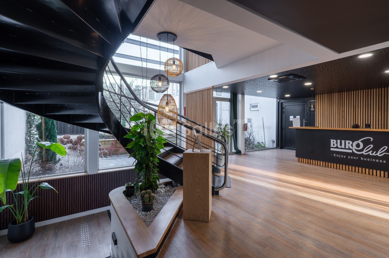 Intérieur moderne d'un espace professionnel avec escalier hélicoïdal noir, accueil en bois et luminaires suspendus dorés.