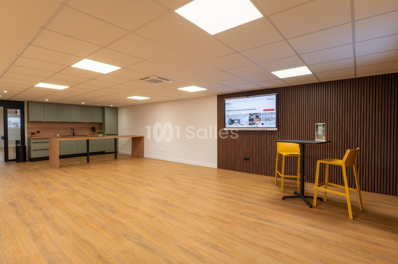 Salle aménagée avec cuisine ouverte, comptoir, écran mural et chaises hautes jaunes - sol parquet.