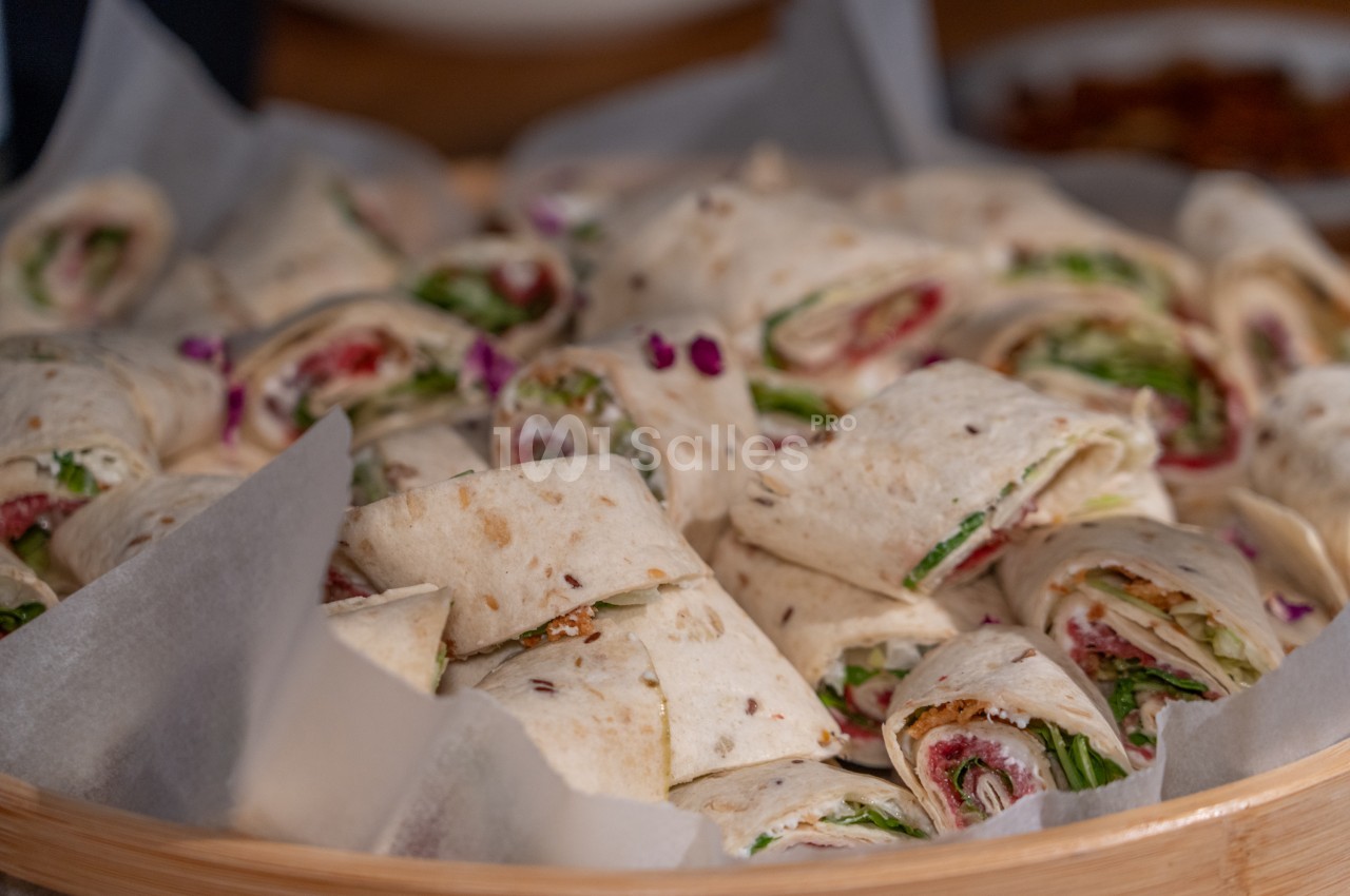 Wraps et sandwiches garnis de légumes et viandes, emballés dans du papier, présentés dans un plateau en bois.