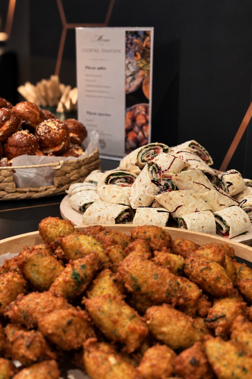 Buffet de présentoir avec boulettes épicées, wraps garnis et beignets dorés en premier plan, menu en arrière-plan.