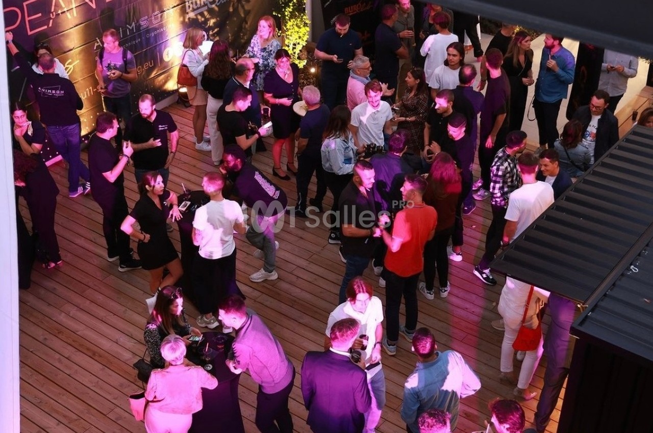Soirée dansante en terrasse sur plancher bois avec éclairage rose-violet et environ 40 convives.