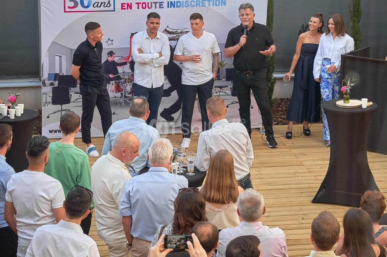 Événement d'entreprise en salle - animateurs sur scène face à un public assis autour de tables.
