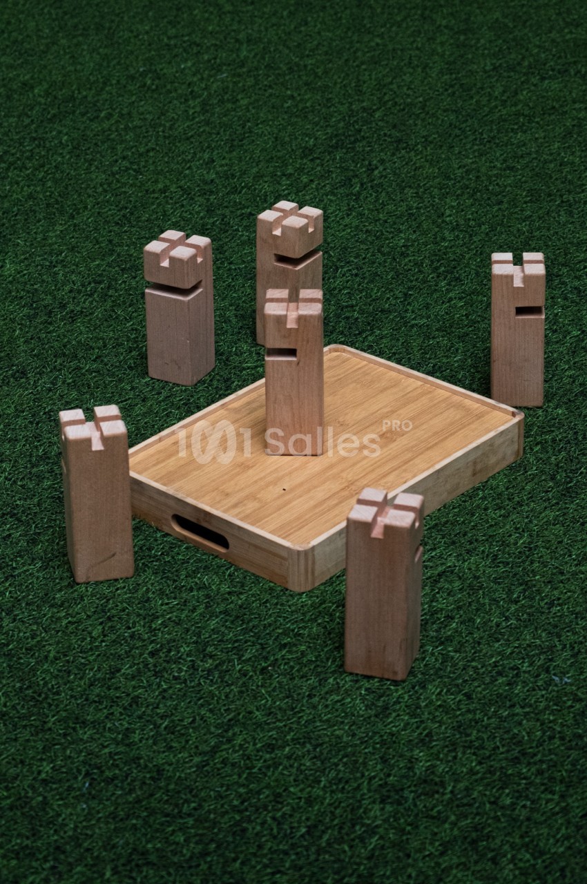 Jeu de kubb en bois avec plateau central et pièces debout sur gazon synthétique.