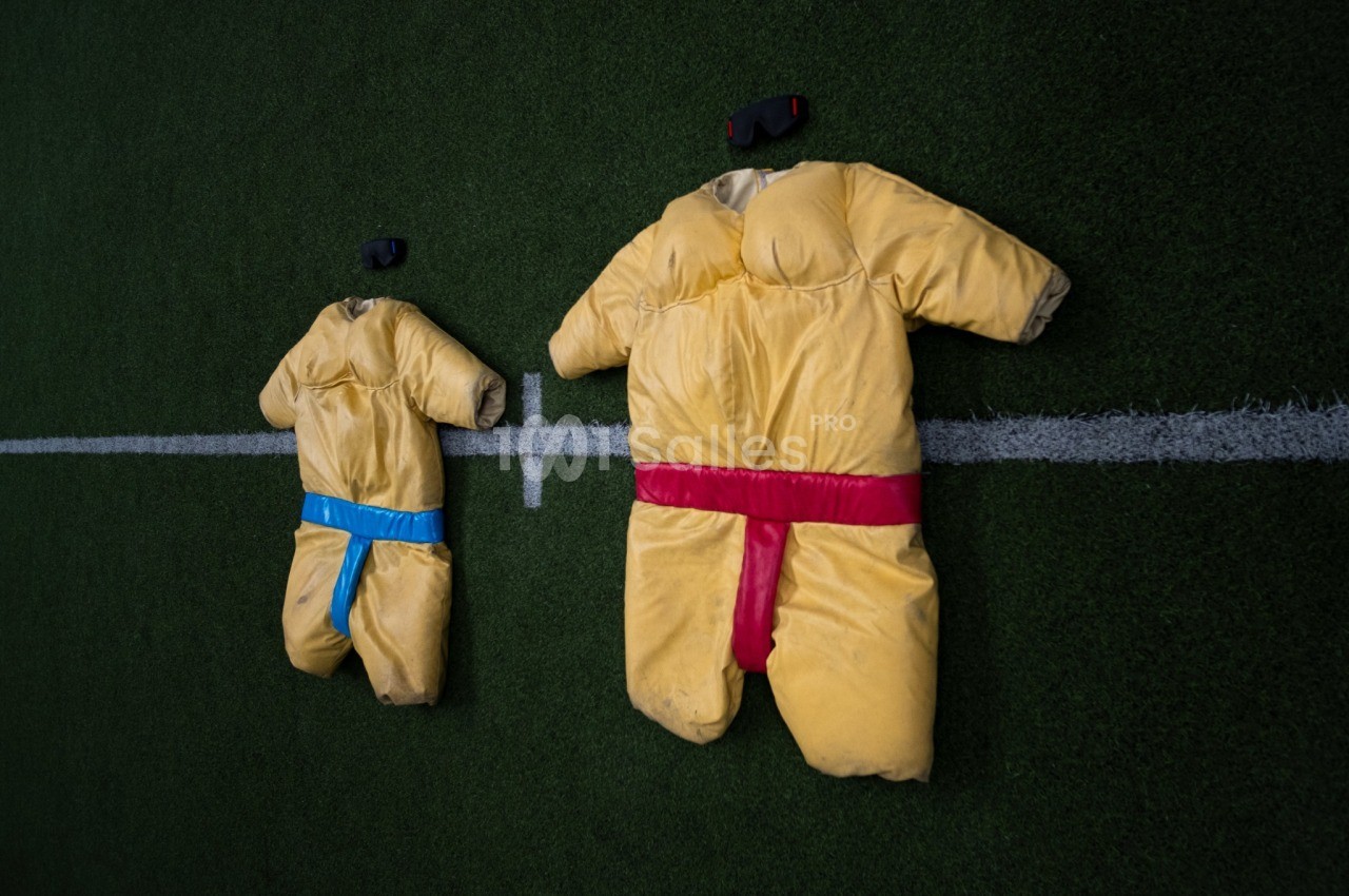Vue aérienne de deux mannequins en tenues de karaté jaunes avec ceintures bleue et rouge sur tapis vert.