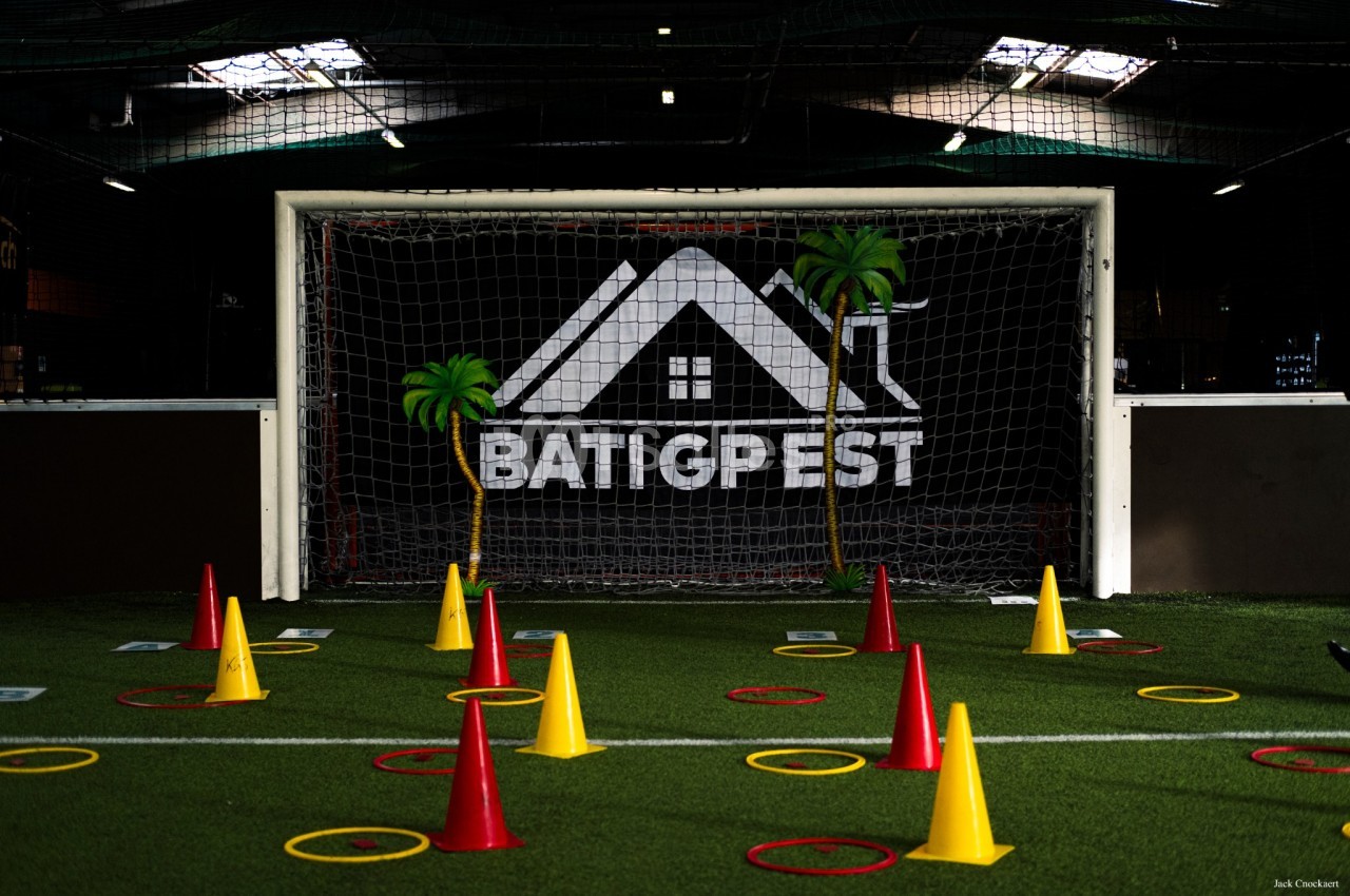 Terrain de football en salle avec un but marqué du logo Batigpest, cônes jaunes et rouges, anneaux au sol pour parcours d'équipe.