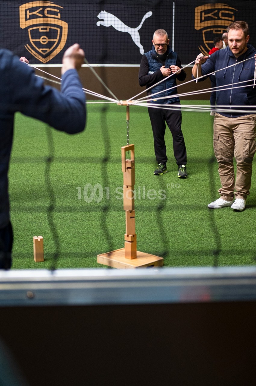 Participants à un jeu de team-building en intérieur avec gazon synthétique et mur de logos.