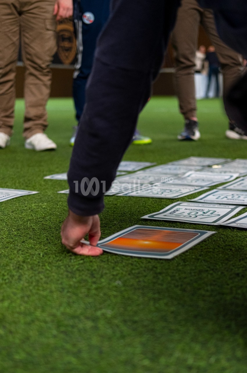 Participants rangent des cartes colorées sur un terrain synthétique vert lors d'une activité de groupe.