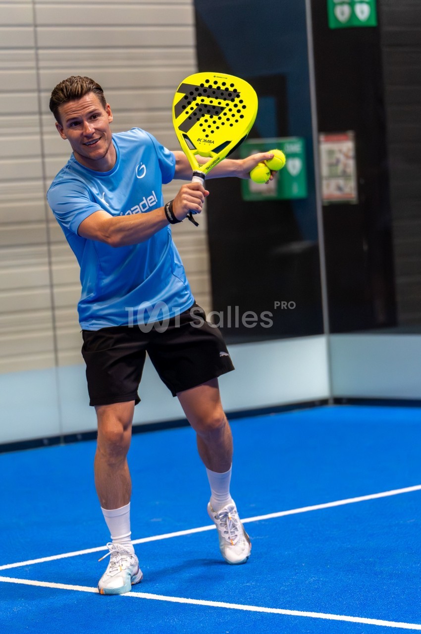 Joueur de padel sur court intérieur bleu avec raquette jaune et balles - aménagement sportif.