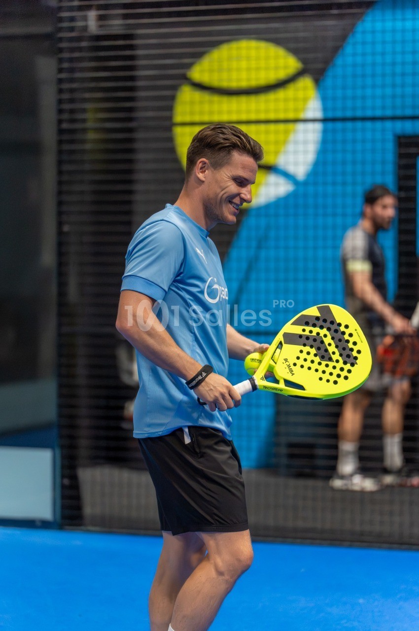 Homme en tenue de sport tenant une raquette de padel jaune sur un court bleu.