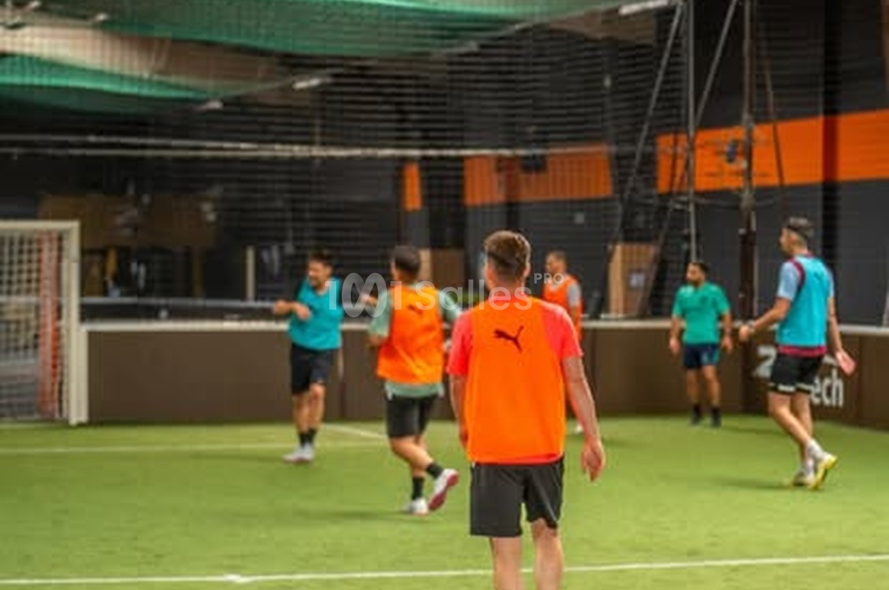 Matchs de football en cours dans un terrain couvert avec murs noirs et orange, filet blanc visible à gauche.