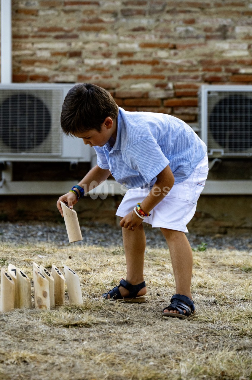 Enfant jouant au jeu de quilles en plein air contre un mur de briques.
