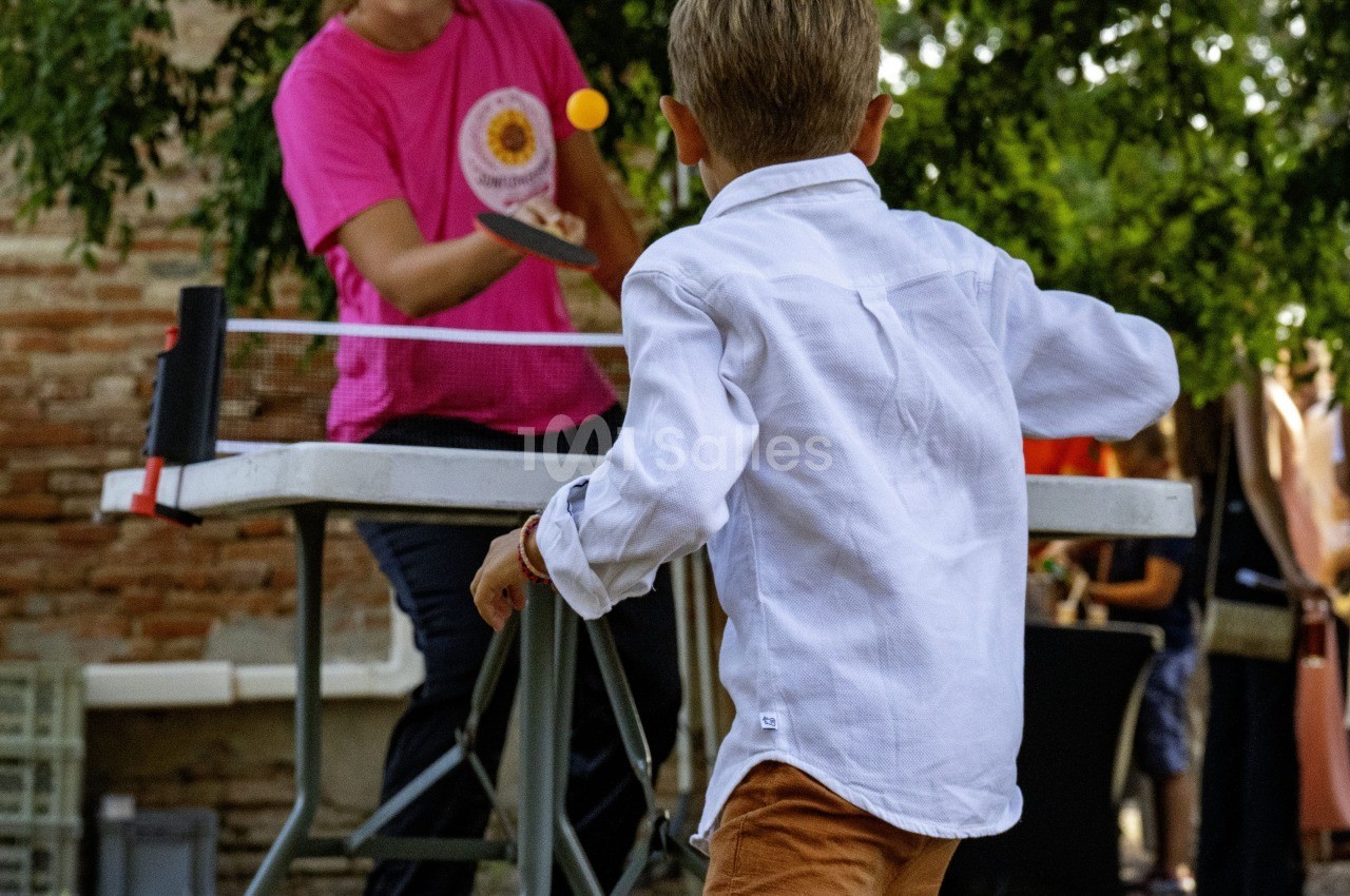 Partie de ping-pong en extérieur dans un jardin avec deux joueurs et filet portable.
