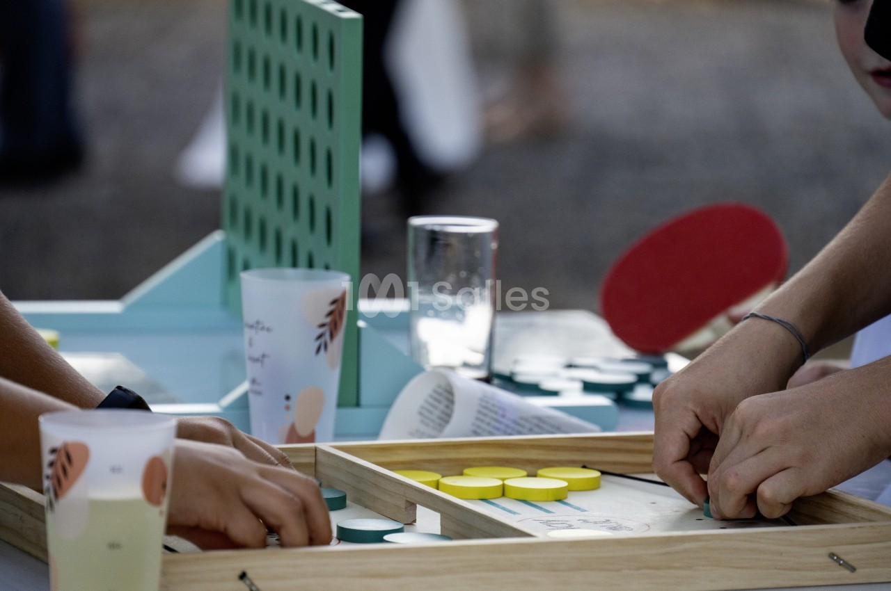 Deux personnes jouent au ping-pong sur table en bois avec raquettes rouges et verres d'eau.