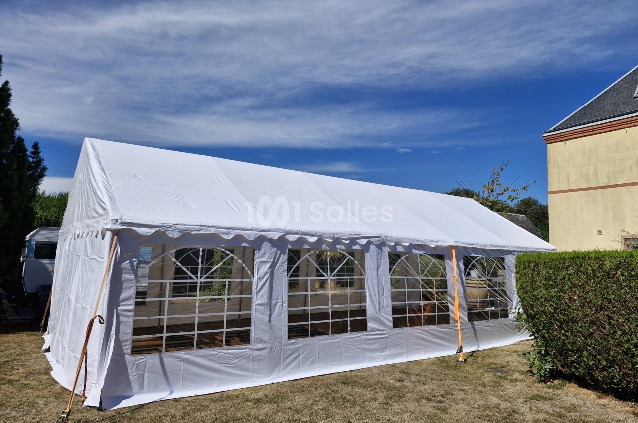 Chapiteau blanc avec parois vitrées dressé en extérieur, ciel bleu en arrière-plan.