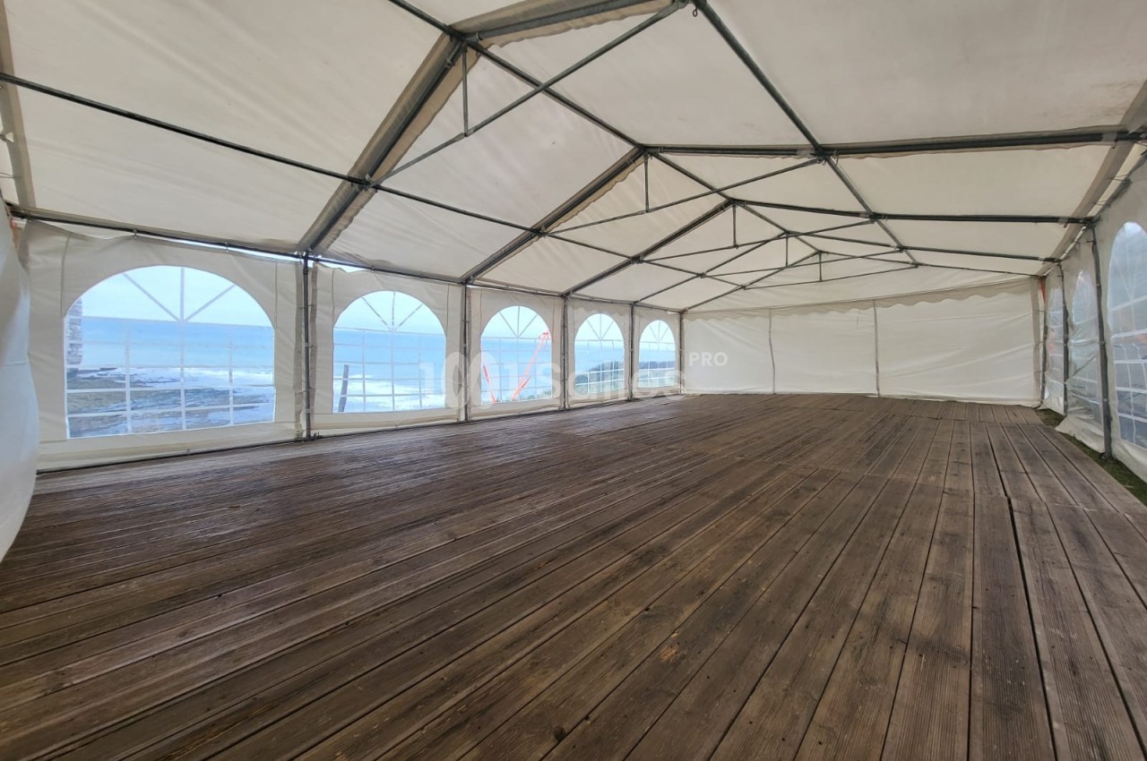 Tente transparente vide avec plancher bois et baies vitrées donnant sur une mer calme.