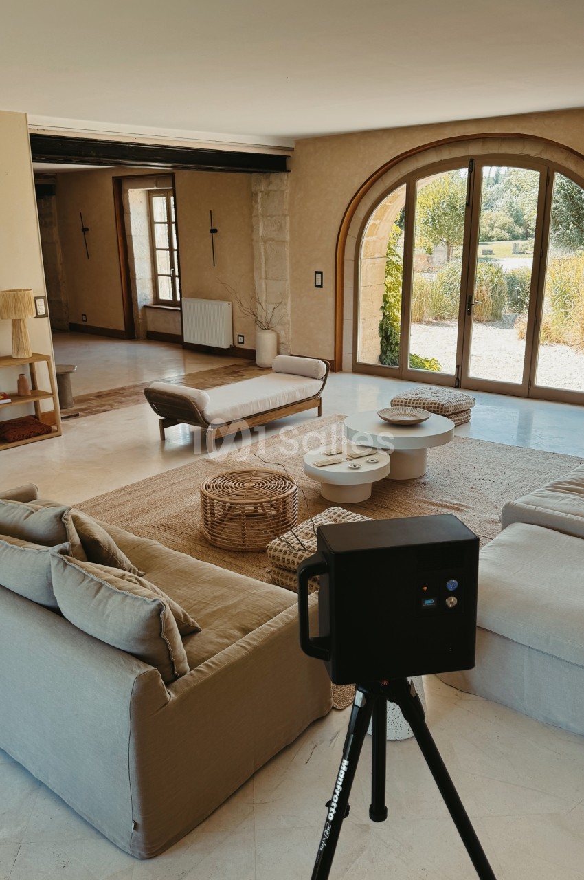 Intérieur spacieux avec canapés beige, table basse blanche et baies vitrées arquées ouvrant sur jardin paysagé.