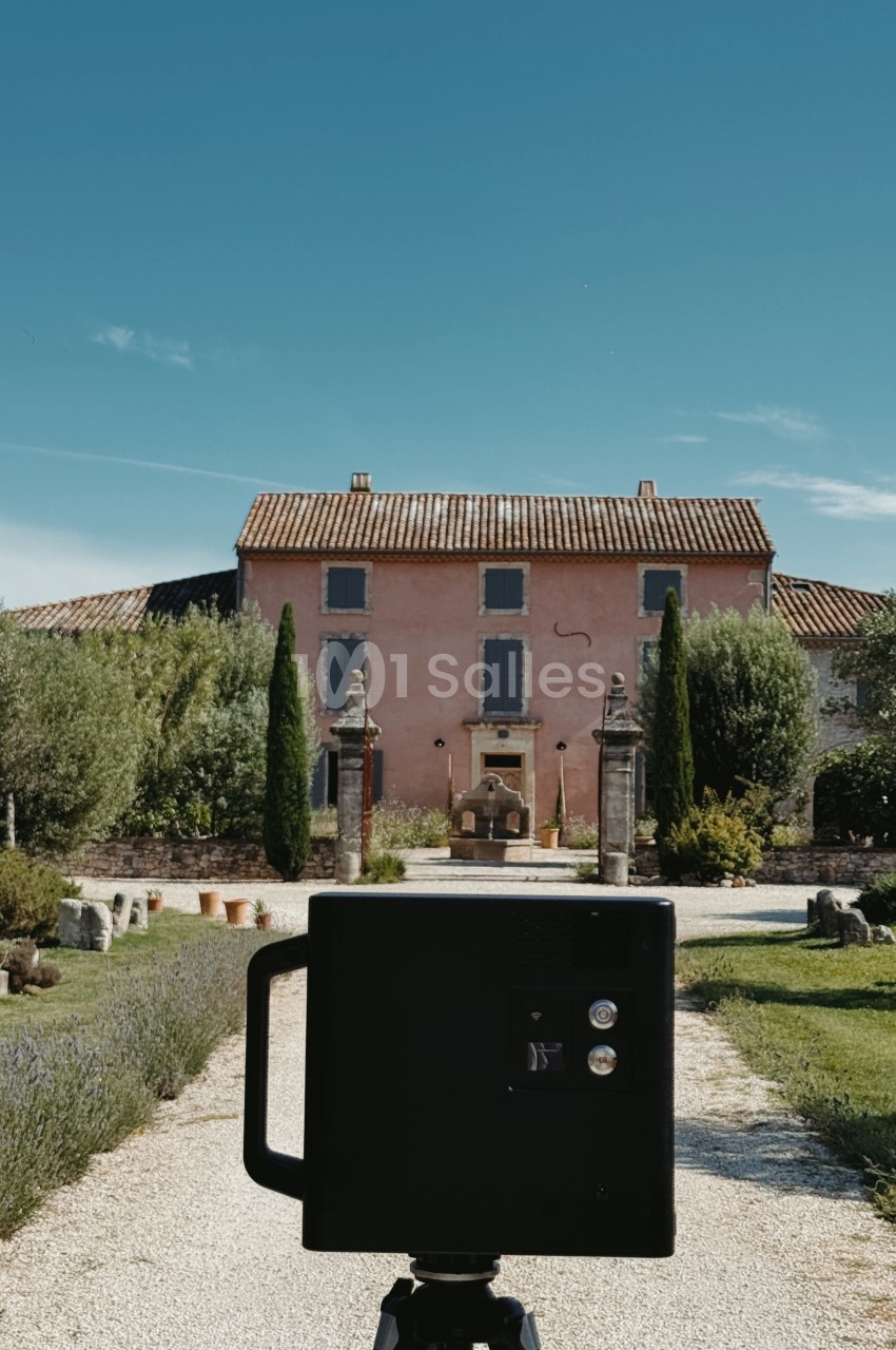 Façade d'une bastide rose provençale avec cyprès, photographiée à travers un appareil photo professionnel sur trépied.