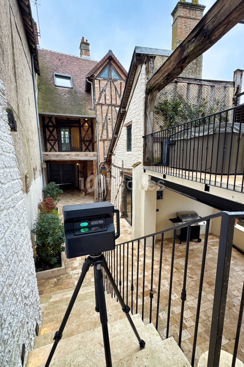 Cour pavée entre bâtisses médiévales à colombages, caméra de tournage sur trépied en premier plan.