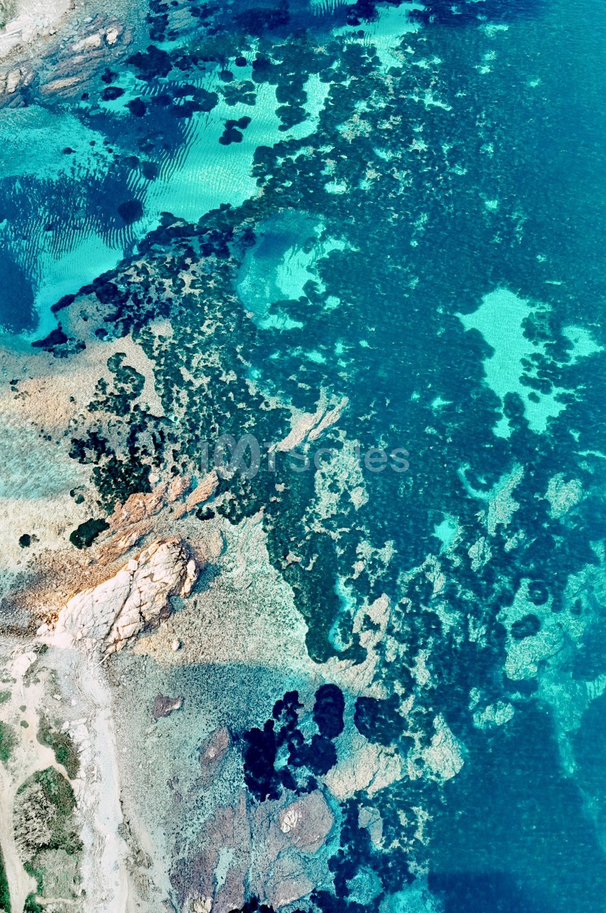 Côte rocheuse et turquoise vue du ciel avec formations de rochers noirs et plage de sable blanc.